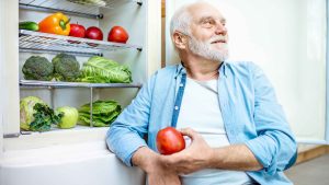 Senior holding an apple with veggie in the background.